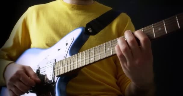 Мужчина-гитарист в желтом джампере играет на электрогитаре на черном фоне — стоковое видео