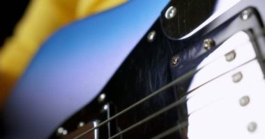 Sarı kazaklı erkek gitarist siyah arka planda elektro gitar çalıyor.