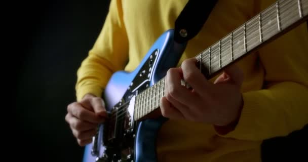 Chitarrista maschile in un maglione giallo suona una chitarra elettrica su sfondo nero — Video Stock