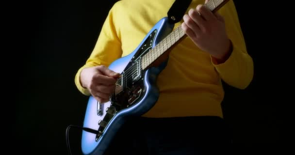 Sarı kazaklı erkek gitarist siyah arka planda elektro gitar çalıyor. — Stok video