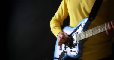 Sarı kazaklı erkek gitarist siyah arka planda elektro gitar çalıyor.