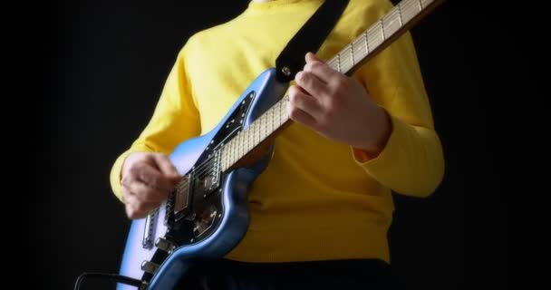 Man gitarrist i en gul jumper spelar en elgitarr på svart bakgrund — Stockvideo