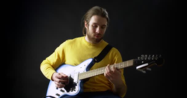 黄色のジャンパーの男性ギタリストは黒を背景にエレキギターを弾く — ストック動画