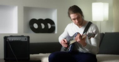 Gri kazaklı yaratıcı müzisyen mavi elektro gitarı akort ediyor.. 