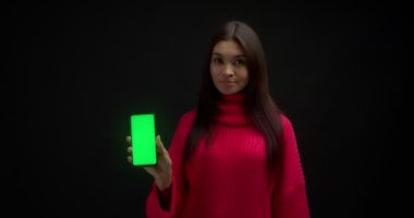Pembe kazaklı kadın kopyalama için dikey yeşil telefon ekranı gösteriyor.