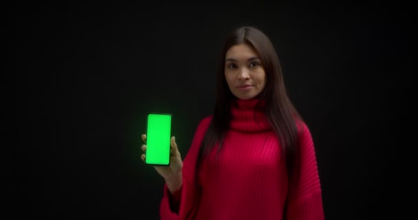 Frau im rosafarbenen Pullover zeigt vertikalen grünen Telefonbildschirm zum Kopieren. — Stockvideo