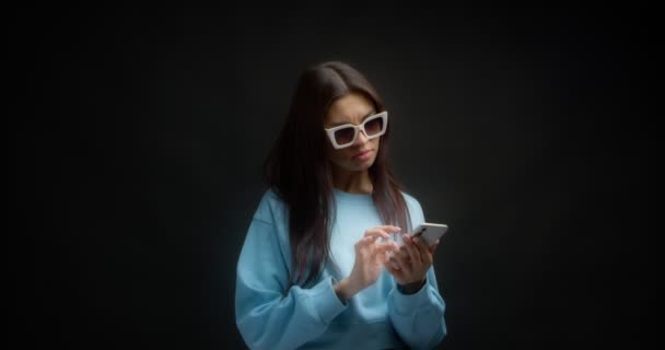 Vrouw met een witte zonnebril denkt na over wat te antwoorden op een chatbericht. — Stockvideo