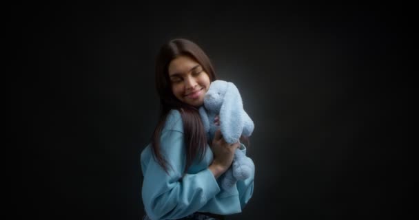 Schattig brunette met lang haar in een blauw jumper knuffels een zacht speelgoed bunny — Stockvideo