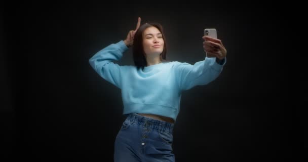 युवा एशियाई महिला एक स्मार्टफ़ोन के सामने चेहरे बनाती है जो मूर्ख सेल्फी लेती है — स्टॉक वीडियो