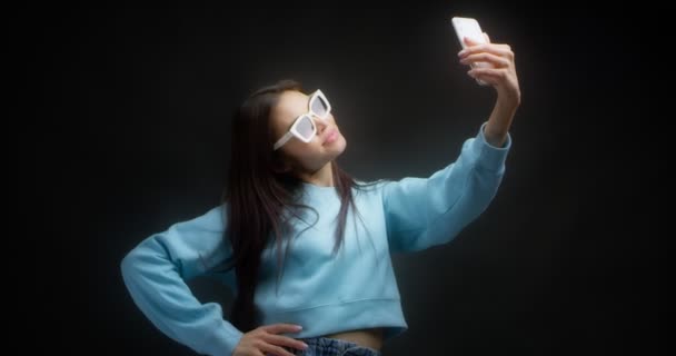 Joven asiática mujer hace caras delante de un teléfono inteligente tomando estúpidos selfies — Vídeos de Stock
