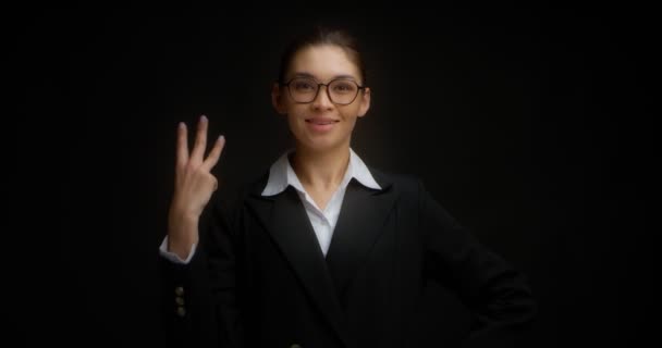 Ασιάτισσα με γυαλιά χαμογελά και δείχνει τρία δάχτυλα με το δεξί της χέρι.. — Αρχείο Βίντεο