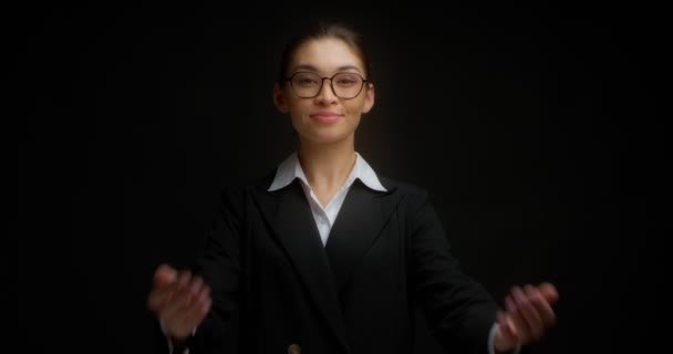 Femme d'affaires dans des lunettes et une veste noire montre un geste de la main venir ici. — Video