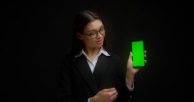 Gözlüklü iş kadını kopyalama için dikey yeşil telefon ekranı gösteriyor. ChromaKey