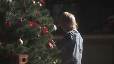 Mutlu küçük çocuk Noel ağacını süslüyor ve evde yeni yılın tadını çıkarıyor. Noel Baba şapkalı şirin yalnız çocuk toplarını sallıyor. Aile kavramı ile kış tatili