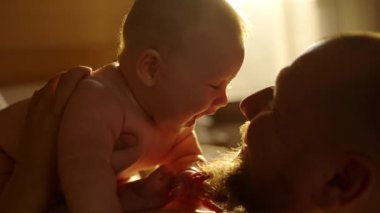 Sakallı, yeni doğmuş bebeğini okşayan ve öpen genç bir baba. Annesi tarafından sabah mutfakta kollarında tutuluyor. Aile kavramı, babalık, annelik, ebeveynlik, çocukluk, yaşam.