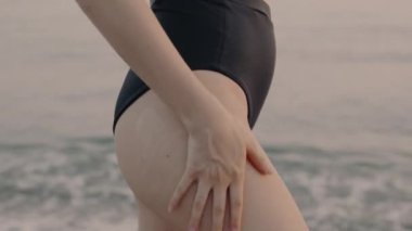 Deniz kenarındaki kadın kalçasına nemlendirici krem sürüyor. Vücut pozitif. Kalçalara güneş kremi sürmeye yakın. Doğal güzellik kavramı