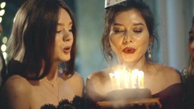 Partide ya da doğum günü şapkalı Asyalı bir kız evinde ya da evinde tatil partisinde dilek diliyor. Doğum günü pastasında mum üfleyen ve tebrik eden çok ırklı genç bayan arkadaşlarının portresi..