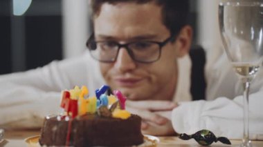 Gözlüklü, üzgün, kafkasyalı adamın yakın plan yüzü. Evde, pastaların önünde, mumlarla tek başına oturmuş, hamur işi yiyor. Yalnızlıkta parti ya da kutlama.