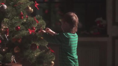 Mutlu küçük çocuk Noel ağacını süslüyor ve evde yeni yılın tadını çıkarıyor. Noel Baba şapkalı sevimli yalnız çocuk dekorasyonlara dokunuyor. Aile kavramı ile kış tatili