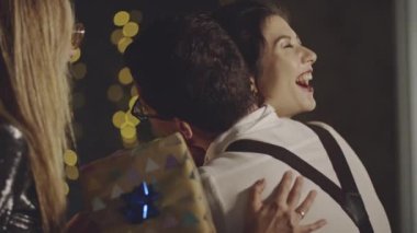 Neşeli bir kadın arkadaşlarıyla kucaklaşıp tokalaşıyor, doğum günü için kağıda sarılmış hediyeler alıyor ve akşam yemeğinden önce evde teşekkür ediyor. Parti ya da doğum günü kutlaması şirket ya da grupla.