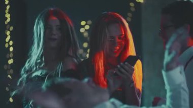 Partide dans ederken telefona bağımlı beyaz sarışın bir kızın portresi. Genç bir kadın modern teknoloji kullanarak internet üzerinden iletişim kuruyor. Dans eden ve ona müdahale eden arkadaşlar..