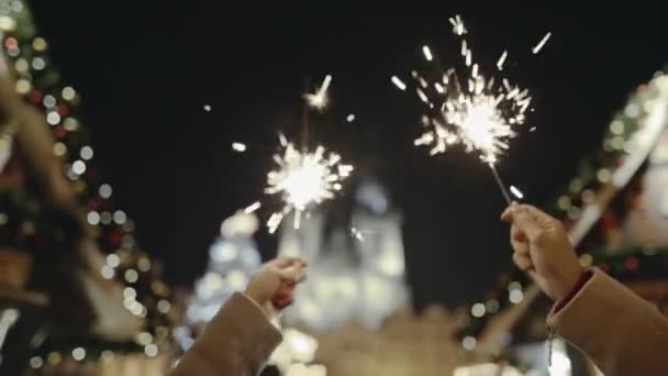 In the foreground tender female hands with brightly burning bengal lights. In the background Christmas street fair with wonderful festive decarations and various items. Concept of festival. Copy space — Stock Footage In the foreground tender female hands with brightly burning bengal lights. In the background Christmas street fair with wonderful festive decarations and various items. Concept of festival. Copy space Royalty Free Stock Footage