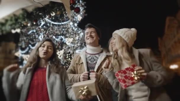 Three friends dancing with gifts in hands at xmas night at old town square. Friendship, christmas, new year, holiday concept. Filmed on RED camera, 10 bit clolor — Stock Footage Three friends dancing with gifts in hands at xmas night at old town square. Friendship, christmas, new year, holiday concept. Filmed on RED camera, 10 bit clolor Stock Footage