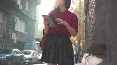 Sokakta tablet kullanan şık bir kadın. Gülümseyen kız kamerada flört ediyor. Güzel bir kadın eski şehir sokağına gidiyor ve güneş parlıyor. Mor saçlı, seksi, stil sahibi bir kadın.