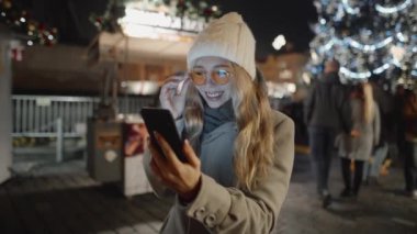 Genç bir kadın noel yemeğinin ortasında telefon ekranına bakıyor. Güzel kız Avrupa 'da seyahat ederken sohbet ediyor ya da video görüşmesi yapıyor..