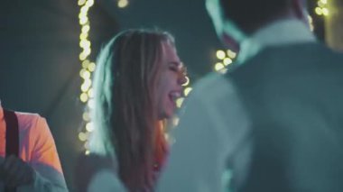 Mutlu, gülümseyen adamlar renkli ışıklarla süslenmiş evin önünde birlikte eğleniyorlar. Doğum gününde, yeni yılda, Noel 'de ya da Xmas partisinde dans eden çok ırklı genç hippi arkadaşlara yakın çekim.