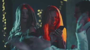 Partide dans ederken telefona bağımlı beyaz sarışın bir kızın portresi. Genç bir kadın modern teknoloji kullanarak internet üzerinden iletişim kuruyor. Dans eden ve ona müdahale eden arkadaşlar..