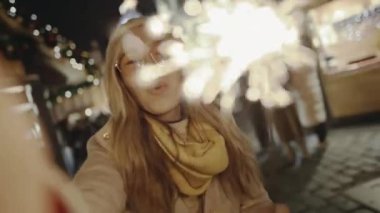 Yeni yıl arifesinde gülümseyen ve yanan parlak kıvılcımlar. Selfie zamanı, kız blogcu Prag Meydanı 'ndaki sokak fuarında sosyal sayfası için video ve fotoğraf çekiyor..