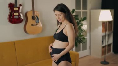 Genç bir anne hamileliğinin tadını evde çıkarıyor. İç çamaşırı giyen güzel Asyalı hamile kadın kameraya bakıyor. Annelik ve aile kavramı