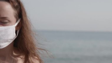 Halk plajında koruyucu maske takan genç bir kadının yarım portresi. Koronavirüse karşı önlem kavramı. Salgın sırasında sağlık ve güvenlik hayatı, N1H1