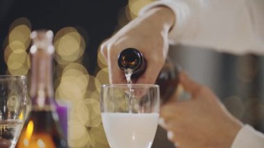 Şampanya şişesinden köpüklü bardaklara köpüklü köpüklü şarap döken ellerin yakın plan çekimi. Yılbaşında, doğum gününde, Noel arifesinde ya da Xmas 'ta kutlama yapan çok ırklı arkadaşlar..