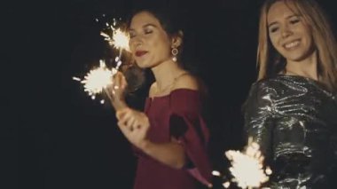 Asyalı ve beyaz kızlar birlikte dans ediyor, ellerinde parlak maytaplar sallıyorlar. Mutlu kız arkadaşlar akşamları ya da akşamları rahatlıyor ve eğleniyorlar. Neşeli kadınlar şenlik partisinde yalnız eğleniyorlar..