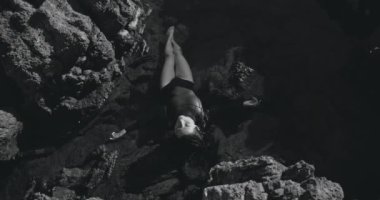 Siyah ve beyaz atış, dişi serbest dalgıç okyanus yakınlarındaki kayalara uzanıyor. Sinema kamerasında çekildi, 12 bit renk.