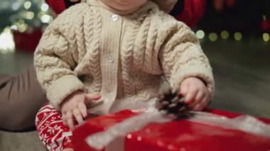 Annem bebeğine kırmızı bir Noel şapkası takıyor. Aile Kış Gecesini Evde Geçiriyor. Küçük Çocuk 'la Genç Anne oynuyor. Ağır çekim. Noel, Yeni Yıl, Kış Tatili Kutlaması. 4K, 10 bit renk