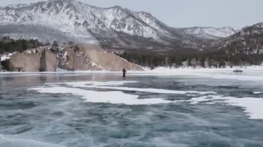 Baykal Gölü 'nde kayan adamın buzla kaplı görüntüsü. Erkek sporcu, soğuk havada, gökyüzü ve bulutlar gölün güzel buzlu yüzeyine yansıyor..