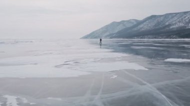 Baykal Gölü 'nde kayan adamın buzla kaplı görüntüsü. Erkek sporcu, soğuk havada, gökyüzü ve bulutlar gölün güzel buzlu yüzeyine yansıyor..