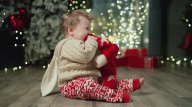 Tavşan kazaklı neşeli bebek kırmızı şapkalı, davullu ve yeni yılın tadını çıkarıyor. Aile Kış Gecesini Evde Geçiriyor. Küçük Çocuk 'la Genç Anne oynuyor. Noel, Yeni Yıl, Kış Tatili