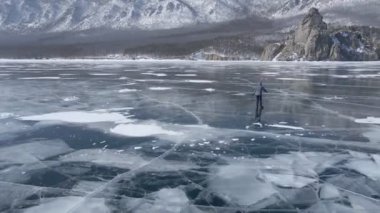 Baykal Gölü 'nde kayan adamın buzla kaplı görüntüsü. Erkek sporcu, soğuk havada, gökyüzü ve bulutlar gölün güzel buzlu yüzeyine yansıyor..