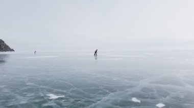Baykal Gölü 'nde kayan adamın buzla kaplı görüntüsü. Erkek sporcu, soğuk havada, gökyüzü ve bulutlar gölün güzel buzlu yüzeyine yansıyor..