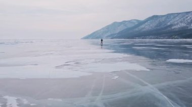 Baykal Gölü 'nde kayan adamın buzla kaplı görüntüsü. Erkek sporcu, soğuk havada, gökyüzü ve bulutlar gölün güzel buzlu yüzeyine yansıyor..