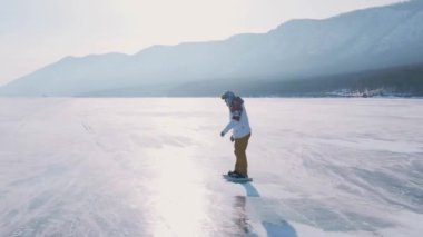 Baykal Gölü 'nde kayan adamın buzla kaplı görüntüsü. Erkek sporcu, soğuk havada, gökyüzü ve bulutlar gölün güzel buzlu yüzeyine yansıyor..