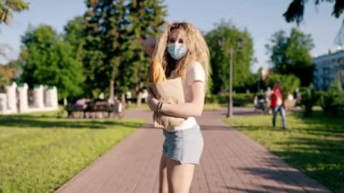 Beyaz, genç, güzel bir kadın, sağlık maskeli bir teslimatçı sokakta yürüyor ve içinde taze yiyecek olan bir paket taşıyor. Dişi güzel kurye markete gidiyor. Genç Asyalı kadın hareket eden maske