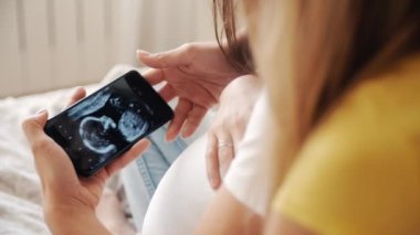 Güzel hamile bir kadın kucağında ultrason fotoğrafı ve yeni doğmuş bir bebekle yatak odasında kız arkadaşıyla birlikte. Aile, kadın aşkı ve romantik ilişki. Güzel Asyalı dostumuz evde.