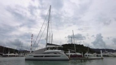 Lüks yelkenli katamaran bir yat limanında duruyor, rıhtımda bir yelkenli yatının yan görüntüsü.