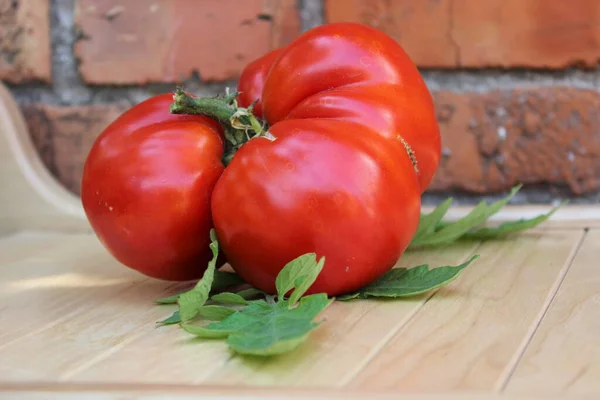 .Grande tomate vermelho em tábuas de madeira no fundo da parede de tijolo. — Fotografia de Stock