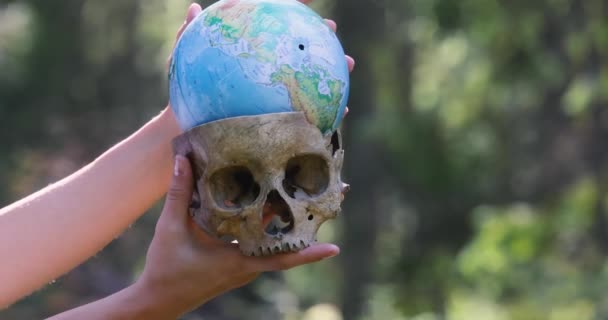 偽の人間の頭蓋骨 装飾用の頭蓋骨 若い女性の手の上に人工の人間の頭蓋骨と小さな地球 モスだ 生態学的概念 高品質4K映像 — ストック動画